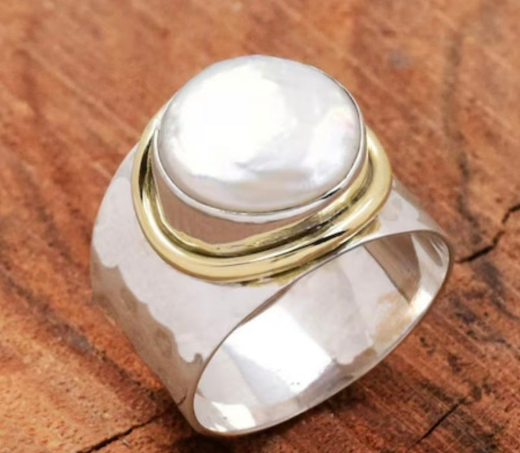A silver ring with a large, smooth white pearl-like cabochon and polished gold accent bands.