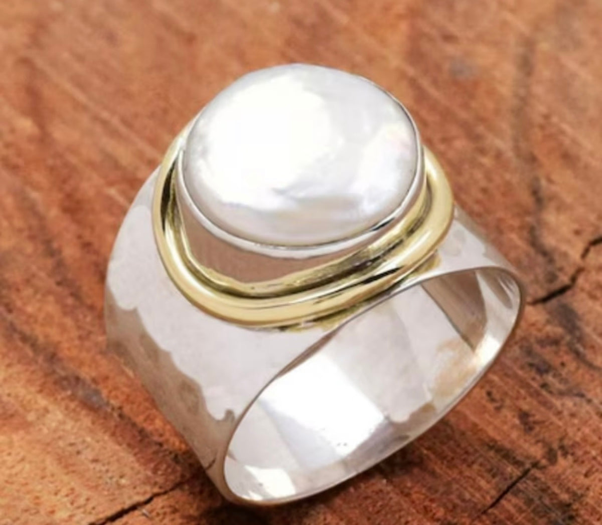 A silver ring with a large, smooth white pearl-like cabochon and polished gold accent bands.